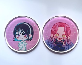 May include: Two round, clear acrylic pins featuring anime-style illustrations. One pin has a character with black hair and blue highlights, the other has a character with pink hair and blue highlights. Both have a pink background with a grid pattern.