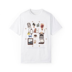 Könnte beinhalten: Weißes T-Shirt mit einem grafischen Druck einer Sammlung von Vintage-Objekten, darunter ein Globus, eine Schreibmaschine, eine Tasse Kaffee, ein Buch, ein Spiegel, ein Blumenstrauß, ein Gemälde und ein Kompass. Der Text "All is fair in love, and poetry" ist unter dem Grafikdruck aufgedruckt.