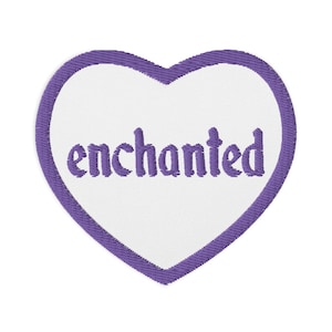 Peut inclure: Patch en forme de cœur violet avec le mot "enchanté" brodé en blanc.
