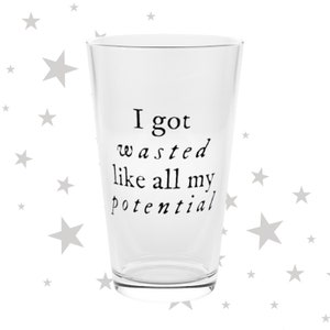 May include: A clear glass pint glass with black text that reads "I got wasted like all my potential." The glass is empty and set against a white background with gray star shapes.