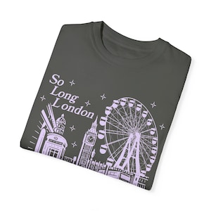 Könnte beinhalten: Ein dunkelgraues T-Shirt mit einem hellvioletten Design von Londoner Sehenswürdigkeiten, darunter Big Ben, ein Riesenrad und ein Gebäude mit einem Uhrturm. Der Text "So Long London" ist auf dem Shirt aufgedruckt.