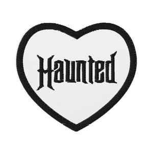 May include: White heart-shaped patch with a black outline and the word "Haunted" embroidered in black.