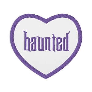 Puede incluir: Parche morado en forma de corazón con la palabra "haunted" bordada en blanco.