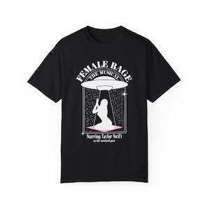 Könnte beinhalten: Schwarzes T-Shirt mit einem weißen Grafikdesign, das eine Frau zeigt, die unter einem UFO kniet. Der Text "Female Rage The Musical Starring Taylor Swift as the tortured poet" ist auf dem Shirt aufgedruckt.