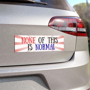 May include: A rectangular bumper sticker with the text "NONE OF THIS IS NORMAL" in red, black, and blue. The text is set against a white background with red and white rays emanating from the center.