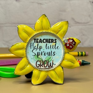 May include: A yellow sunflower-shaped metal frame with a round center featuring the text "TEACHERS Help little Sprouts GROW" and a red ladybug with rhinestones.