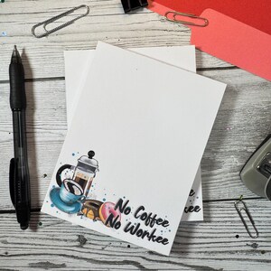 May include: Two white notepad stacks with a blue and white illustration of a coffee pot, coffee cup, and donuts. The text "No Coffee No Workie" is written in black on the notepad.