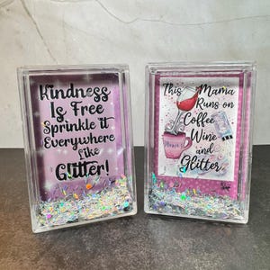 May include: Two clear acrylic blocks with glitter and text. One says "Kindness Is Free Sprinkle it Everywhere Like Glitter!" The other says "This Mama Runs on Coffee Wine and Glitter."