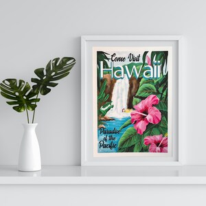 K&ouml;nnte beinhalten: Ein gerahmtes Vintage-Reiseposter mit den Worten "Come Visit Hawaii" und "Paradise of the Pacific". Das Poster zeigt einen Wasserfall, rosa Hibiskusbl&uuml;ten und &uuml;ppiges gr&uuml;nes Laub. Links steht eine wei&szlig;e Vase mit gr&uuml;nen Bl&auml;ttern.