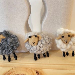 May include: Three felt sheep ornaments, one gray, one light gray, and one white. Each sheep has black eyes, a brown nose, and black legs.