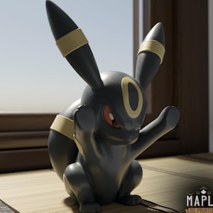 May include: A black and yellow Umbreon figurine with long ears, red eyes, and yellow ring markings on its ears, forehead, and body. The figure is in a seated pose with one arm raised. A logo with the text Maple 3D Printing is visible.