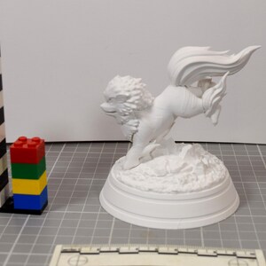 May include: A white, unpainted 3D printed figurine of a mythical creature with a large, flowing tail and a mane, standing on a textured base. A black and white striped tower and a stack of red, green, yellow, and blue plastic bricks are nearby.