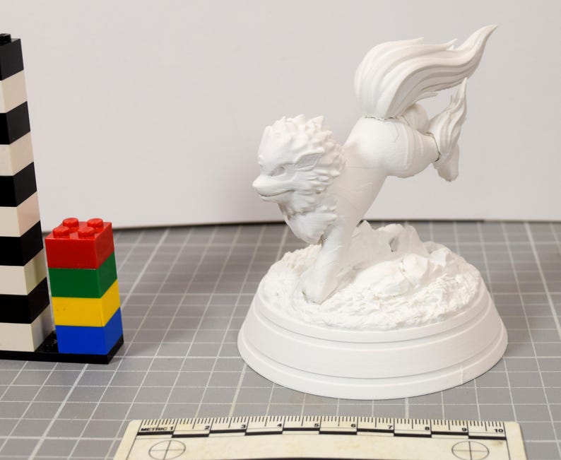 May include: A white, unpainted 3D printed figurine of a four-legged creature with a large, flowing tail and a textured mane, mounted on a circular base. A ruler is visible at the bottom, showing a scale in centimeters for size reference.