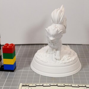 May include: A white 3D printed figurine of a mythical creature with a bushy tail and pointed ears, standing on a textured circular base. A black and white striped tower of building blocks and a ruler measuring up to 10 centimeters are visible.