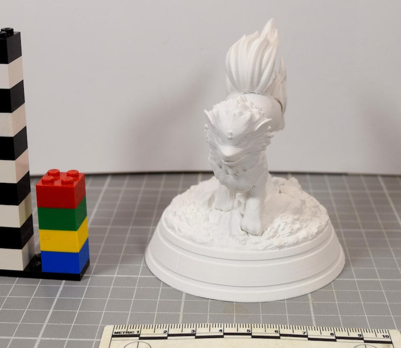 May include: A white 3D printed figurine of a mythical creature with a bushy tail and pointed ears, standing on a textured circular base. A black and white striped tower of building blocks and a ruler measuring up to 10 centimeters are visible.