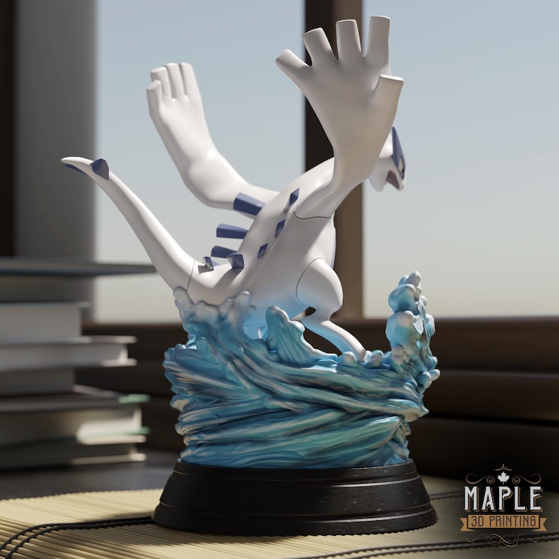 May include: A white and blue Lugia figurine standing on a sculpted blue water base. The creature has large wings, a long tail, and blue dorsal plates. It is mounted on a circular black pedestal with the text MAPLE 3D PRINTING printed on the base.