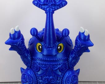 May include: A blue 3D-printed figurine of a stylized insect-like creature with a large horn and ornate detailing. The figurine has yellow eyes and white accents on its claws and feet. The overall design is symmetrical and detailed.
