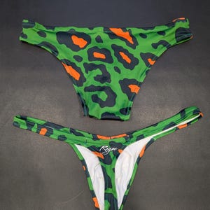 Peut inclure: Deux paires de sous-vêtements à imprimé léopard vert et orange. La paire du haut a une taille plus large et la paire du bas a une taille plus fine avec le mot "Ryze" imprimé au dos.
