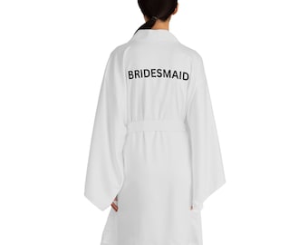 Può includere: Accappatoio bianco con la scritta "BRIDESMAID" in nero sul retro. L'accappatoio ha maniche lunghe e una cintura.