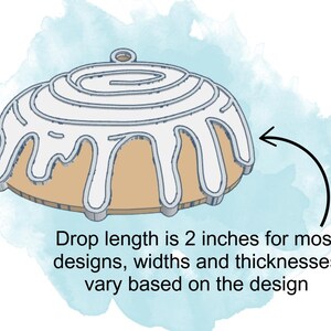 May include: A white icing cinnamon roll ornament with a 2-inch drop length. The ornament is made of wood and is perfect for decorating a Christmas tree or adding a festive touch to any room.