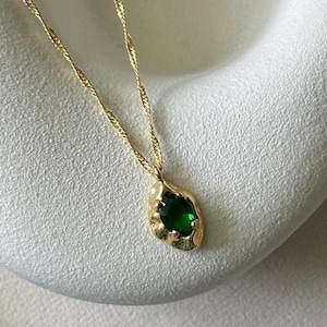 May include: A gold chain necklace with a green gemstone pendant. The pendant is shaped like a teardrop and has a textured, organic design.