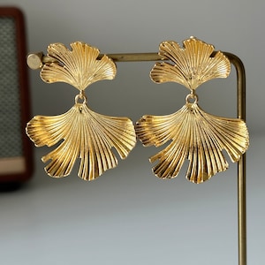 May include: A pair of gold-tone earrings featuring a ginkgo leaf design. The earrings are made of metal and have a shiny finish.