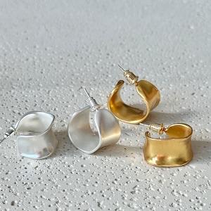 May include: Three pairs of hoop earrings in silver and gold. The earrings are all the same shape, but different sizes. The earrings are on a white textured surface.