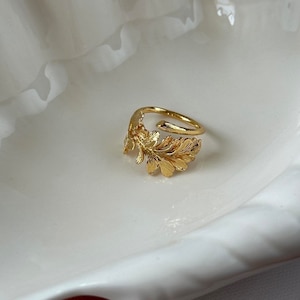 May include: A gold-toned ring with a leaf design. The ring is open and adjustable.