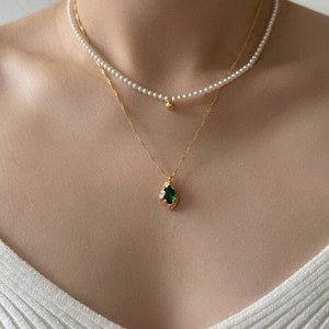 Peut inclure: Un collier en cha&icirc;ne dor&eacute;e avec un pendentif en pierre pr&eacute;cieuse verte et un collier de perles avec un pendentif en boule dor&eacute;e.