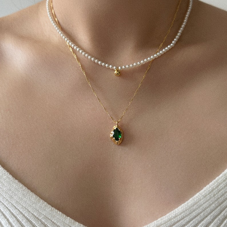 Peut inclure: Un collier en cha&icirc;ne dor&eacute;e avec un pendentif en pierre pr&eacute;cieuse verte et un collier de perles avec un pendentif en boule dor&eacute;e.