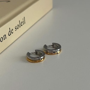 May include: Two silver hoop earrings with a thin gold band around the top of each hoop.