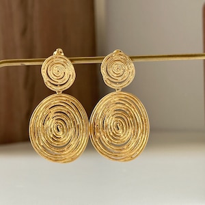 May include: A pair of gold-tone earrings with a double circle design. Each circle is made of a spiral pattern.