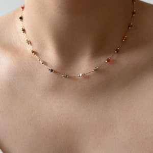 May include: A gold chain necklace with small, colourful beads. The beads are various shades of green, red, purple, and white.