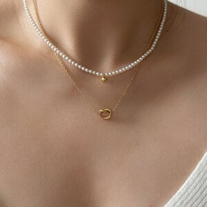 Peut inclure: Un collier superpos&eacute; avec un brin de perles et une cha&icirc;ne en or avec un pendentif en forme de n&oelig;ud.