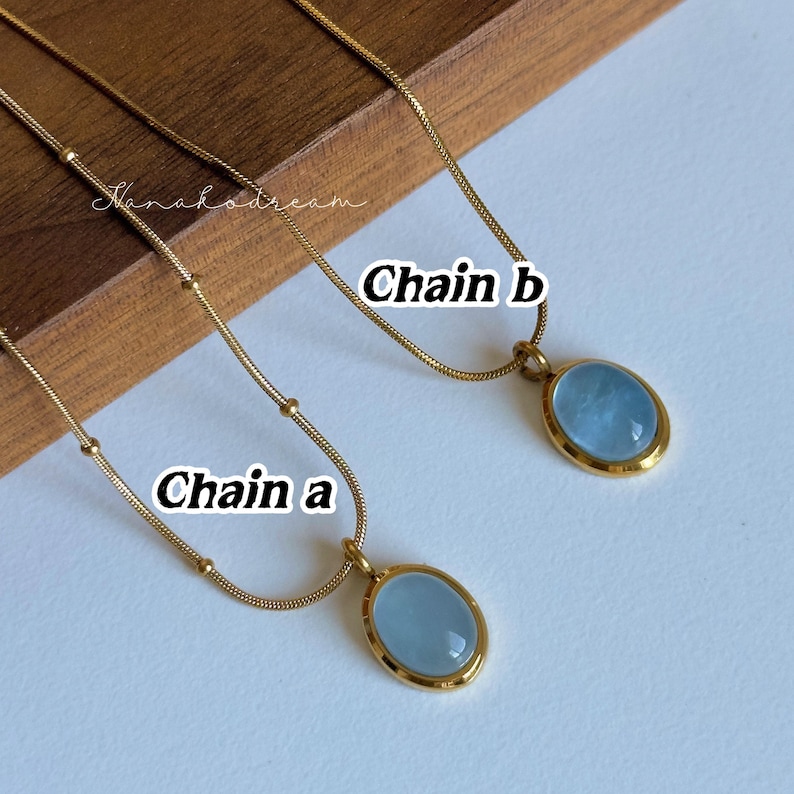 Peut inclure: Deux colliers dor&eacute;s, &eacute;tiquet&eacute;s "Cha&icirc;ne A" et "Cha&icirc;ne B". Chaque collier pr&eacute;sente une cha&icirc;ne fine et un pendentif avec une pierre ovale bleu clair sertie dans un cadre dor&eacute;. L'arri&egrave;re-plan est de couleur claire.