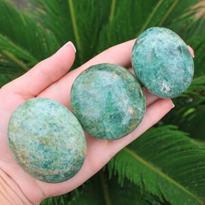 May include: Three smooth, green, polished stones with a mottled pattern. The stones are in the palm of a hand.