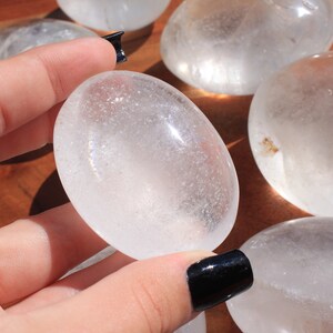 May include: Five smooth, white, oval-shaped clear quartz stones. The stones are polished and have a translucent appearance.
