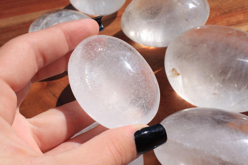 May include: Five smooth, white, oval-shaped clear quartz stones. The stones are polished and have a translucent appearance.