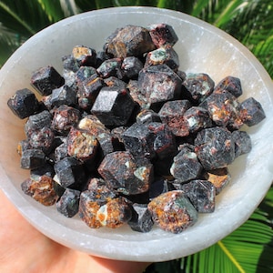 May include: A bowl filled with dark red and black crystals. The crystals are small and have a rough, natural texture.