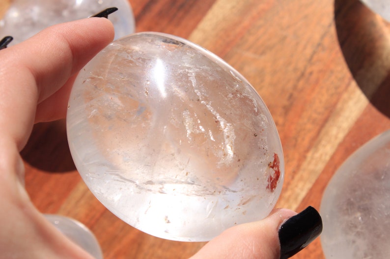 May include: A clear quartz crystal egg with a smooth, polished surface. The egg is translucent and has a slight milky hue. It is approximately 2 inches in diameter.