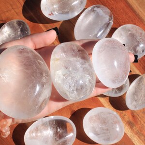 May include: A collection of eight clear quartz crystal tumbled stones. The stones are smooth and polished, with a natural, cloudy appearance.