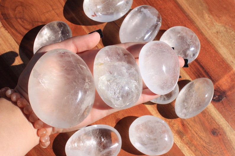 May include: A collection of eight clear quartz crystal tumbled stones. The stones are smooth and polished, with a natural, cloudy appearance.