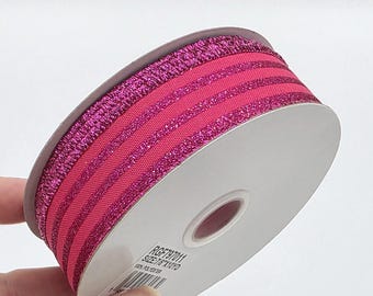 May include: A roll of bright pink ribbon with glitter stripes. The ribbon is wrapped around a white cardboard spool. The text "RGF797011 SIZE 7/8 X10YD" is printed on the spool. The ribbon is likely used for crafts or gift wrapping.