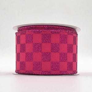 May include: A roll of magenta ribbon with a checkerboard pattern. The ribbon has a textured, glittery finish on some of the squares. The ribbon is on a white spool.