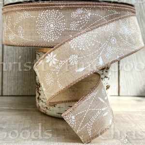 May include: A roll of brown burlap ribbon with a white floral design. The ribbon has a brown edge and is wrapped around a spool.