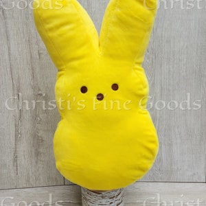 May include: A yellow plush bunny shaped like a marshmallow peep. The bunny is sitting on a white birch log base.