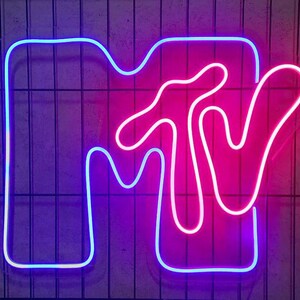 May include: A neon sign in the shape of the MTV logo. The "M" is outlined in blue and the "TV" is outlined in pink.