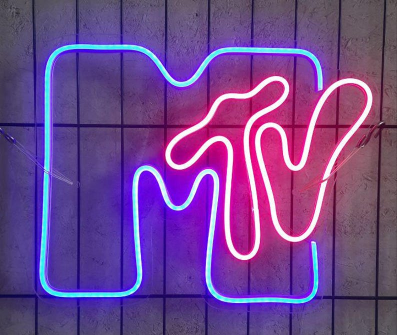 May include: A neon sign with the MTV logo in blue and pink. The sign is made of thin tubing and is lit up.