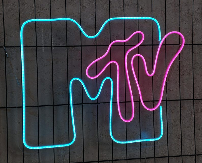 May include: A neon sign with the MTV logo. The "M" is blue and the "TV" is pink.
