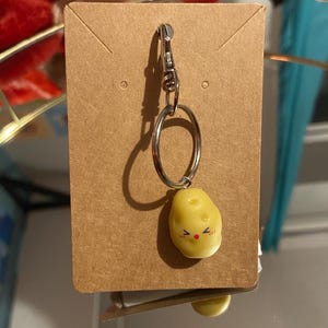 Op de afbeelding: Een bruine kaart met een zilveren sleutelhanger bevestigd aan een gele aardappelhanger met een rood lachend gezicht.